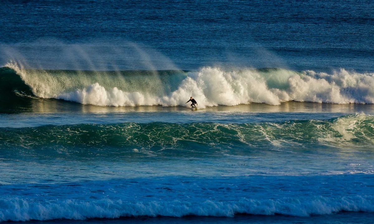 A surfer, catching some waves while being illuminated with late afternoon light at Bells Beach, Australia.